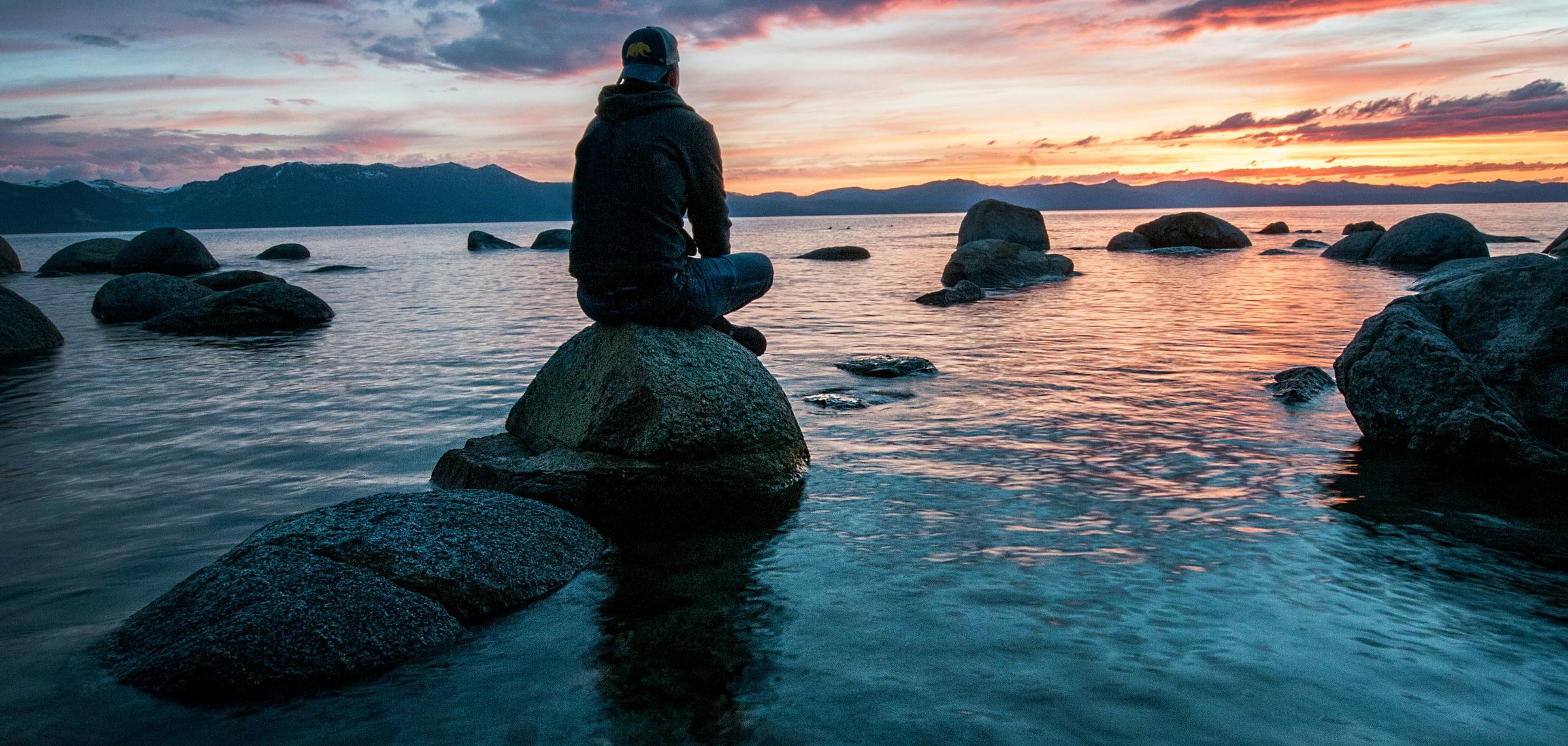 Ein Mensch sitzt ruhig am Wasser im Abendlicht