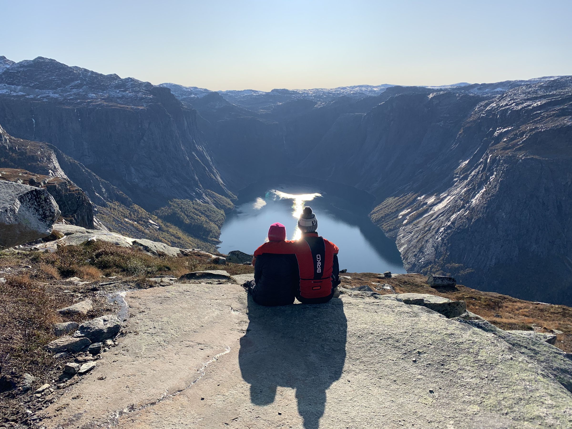 Zwei Menschen sitzen im Morgenlicht über einem Fjord