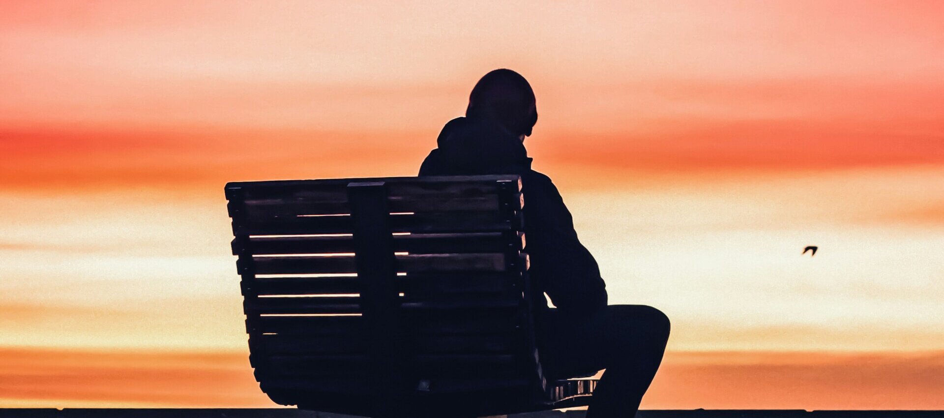 Ein Mensch sitzt allein auf einer Bank bei Sonnenuntergang